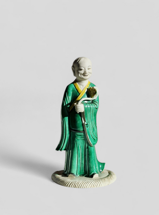 A Chinese sancai-glazed biscuit figure of a Luohan holding a ruyi — Kangxi period (1662–1722)