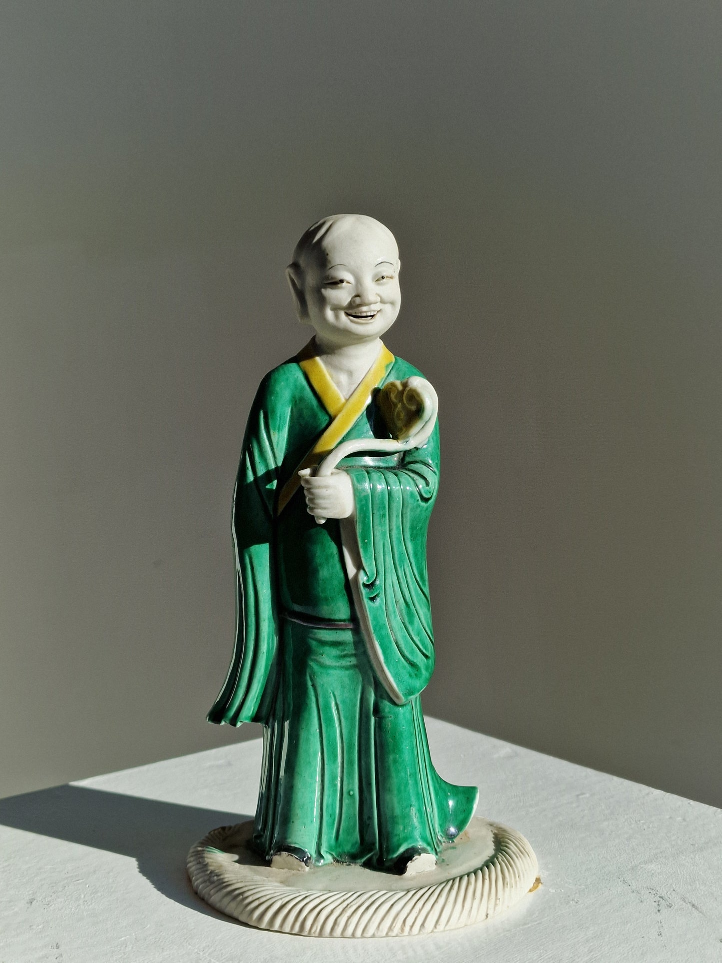 A Chinese sancai-glazed biscuit figure of a Luohan holding a ruyi — Kangxi period (1662–1722)