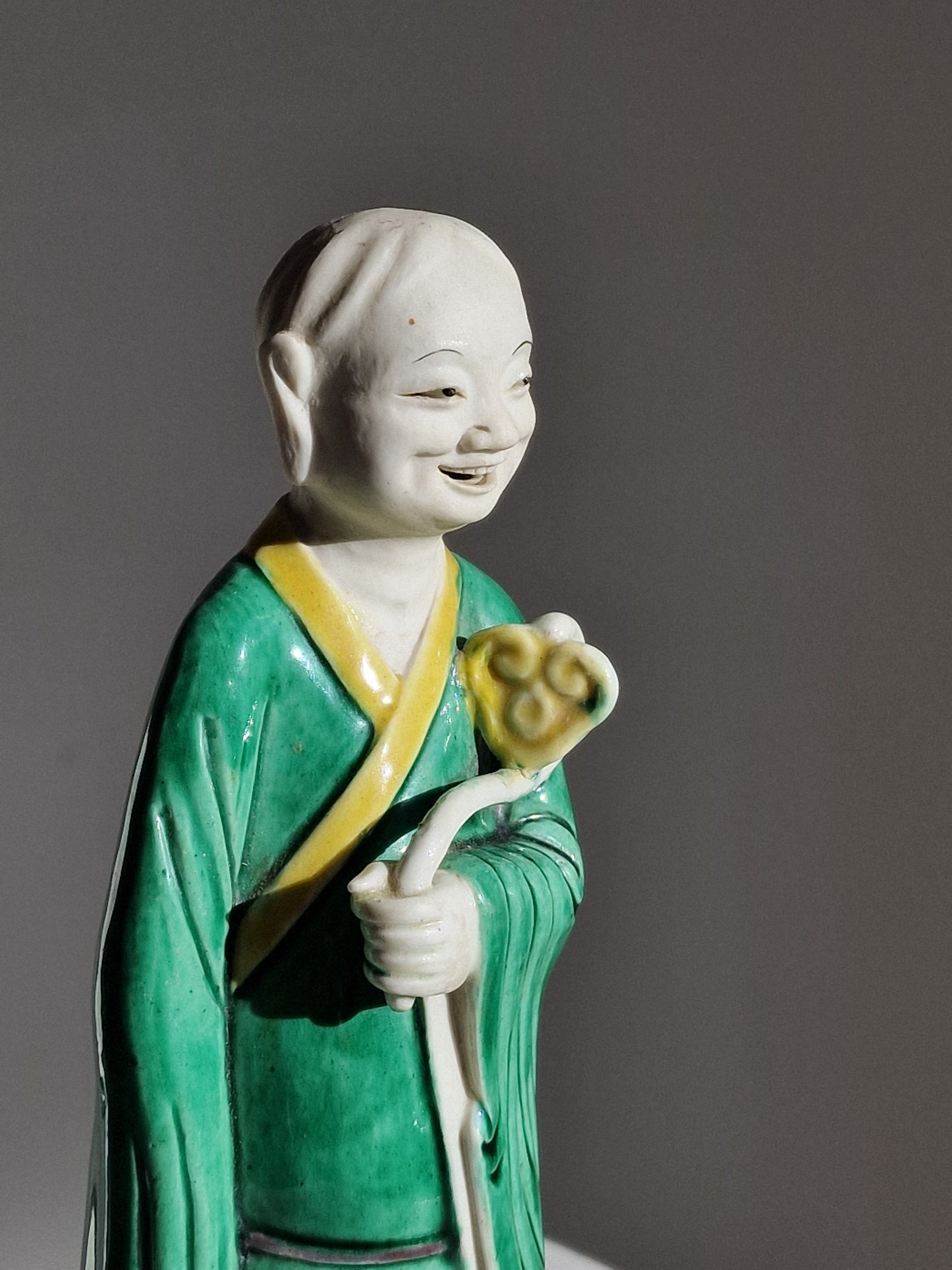 A Chinese sancai-glazed biscuit figure of a Luohan holding a ruyi — Kangxi period (1662–1722)