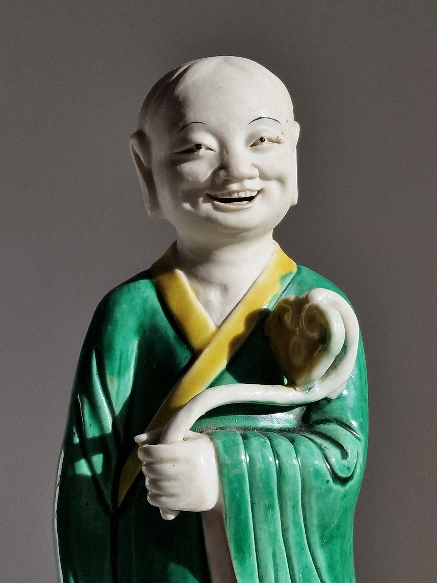 A Chinese sancai-glazed biscuit figure of a Luohan holding a ruyi — Kangxi period (1662–1722)