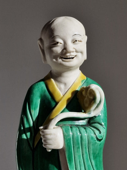 A Chinese sancai-glazed biscuit figure of a Luohan holding a ruyi — Kangxi period (1662–1722)