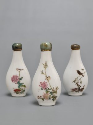 Three Chinese Famille Rose porcelain snuff bottles with green stone stoppers, featuring floral and bird motifs on both sides.
