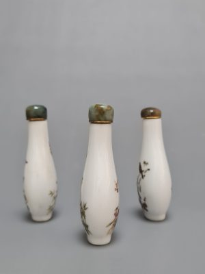 Three Chinese Famille Rose porcelain snuff bottles with green stone stoppers, featuring floral and bird motifs on both sides.